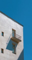 A section of a light beige building with a small balcony against a vibrant blue sky.  A subtle shadow is cast on the building's facade