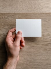 Obraz premium A hand holds a blank white card on a light brown wooden surface