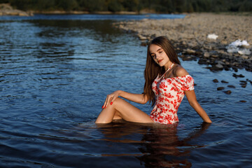 A woman with long dark hair is sitting in the water. She is wearing a purple dress.