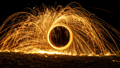 Mesmerising circle and ring of orange fire spark from spinning steel wool. spectacular long exposure light painting effect against dark background creating magical portal
