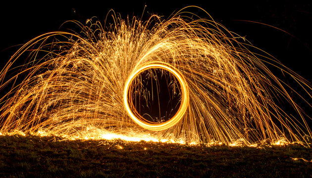 Mesmerising circle and ring of orange fire spark from spinning steel wool. spectacular long exposure light painting effect against dark background creating magical portal