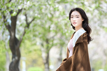 Young Asian female in spring park wearing brown coat and pink dress outdoors