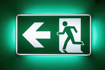 Green Emergency Exit Sign with Low Feedback Directing Evacuation to the Left with a Running Man Symbol in a Building for Safety and Quick Escape