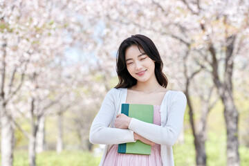 Obraz premium Young Asian female student holding a green book outdoors in spring park