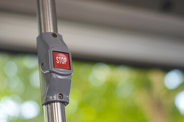 Close-up of a red stop button on a metal pole inside a bus. The button is used by passengers to...