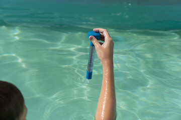 hand holding a thermometer in a swimming pool person holding a blue pool thermometer measuring water temperature on a sunny day in a backyard swimming pool, concept of pool maintenance, summer