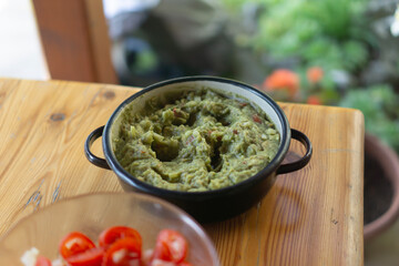 guacamole in a black bowl on a table fresh homemade guacamole with sliced tomatoes on a rustic wooden table prepared for eating on a sunny day outdoors, mexican cuisine, fresh produce, cooking recipes
