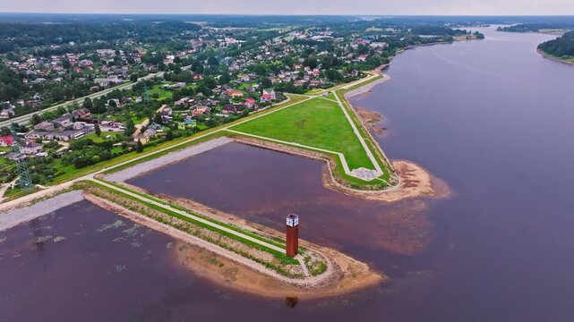 Majestic drone shot showing Ogres lighthouse on riverbank near lush town