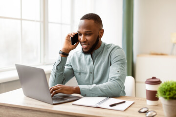 Happy African Business Guy Talking On Cellphone Having Phone Conversation Sitting At Workplace And...