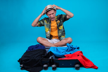 Stressed Young Tourist Man Sitting On An Overflowing Suitcase While Holding His Head In Frustration