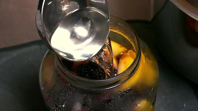 The process of homemade preparation compotes. Housewife pours boiling water into a jar with fruits. Canned sweet fruit lemonades
