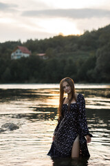 Woman in dark dress at sunset in mountain river on summer day
