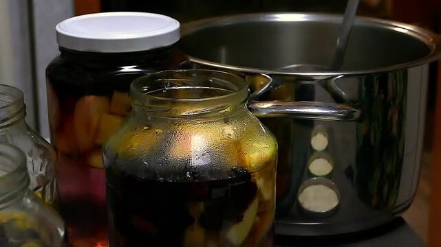 The process of homemade preparation compotes. Housewife pours boiling water into a jar with fruits. Canned sweet fruit lemonades