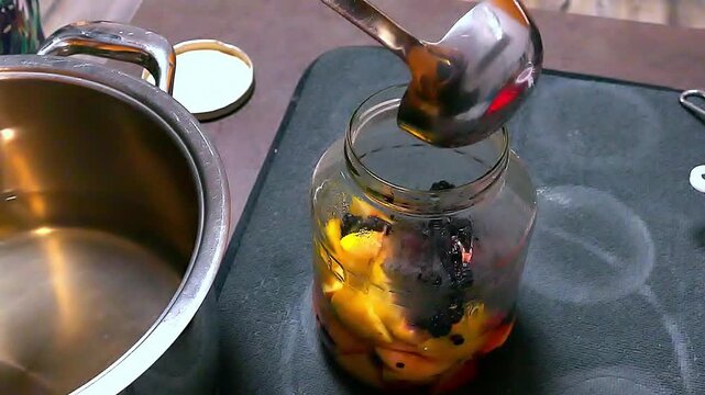 The process of homemade preparation compotes. Housewife pours boiling water into a jar with fruits. Canned sweet fruit lemonades