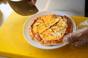The cook is cutting the pizza with a knife on the yellow counter
