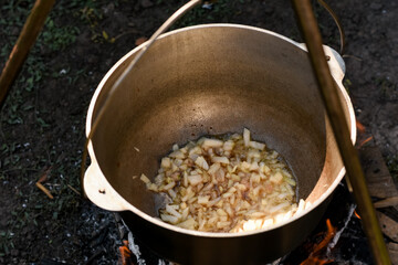 Close-up of onion frying in a cauldron outdoors. Traditional cooking process on open fire, camping...