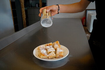 The cook prepares the pastry for service by pouring powdered sugar on it.
