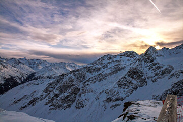Snow-capped mountain peaks at sunset against a dramatic sky in the winter Alps.