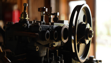 Fototapeta premium A detailed close-up of a vintage industrial machine showcases polished metal gears, a large flywheel, and intricate mechanical parts bathed in warm workshop lighting.