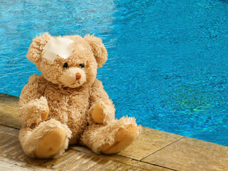 Teddy bear with bandage on head sitting alone beside the swimming pool. Children accident concept
