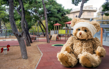 Teddy bear with bandage on head sitting alone on grass at childrens playground. Children safety...