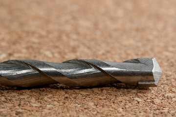 Metal drill bit resting on a textured cork surface in soft lighting