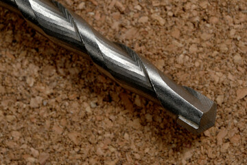 Twisted metal drill bit resting on a textured cork surface
