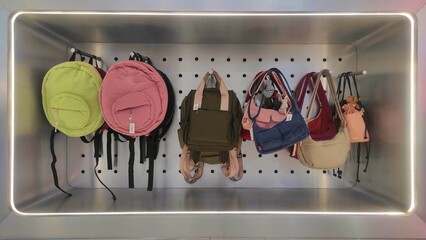 A display of colorful backpacks and handbags hanging neatly on hooks against a modern, illuminated wall, showcasing a variety of styles and designs for shoppers.