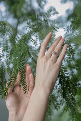 Elegant Woman's Hand with a Sparkling Ring Amidst Lush Green Foliage.