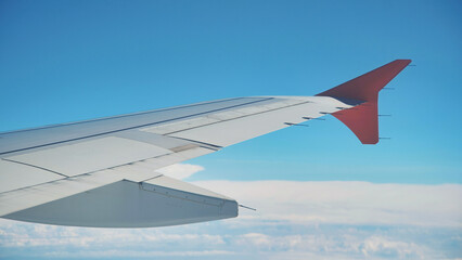 Airplane wing flying above the clouds with blue sky in background