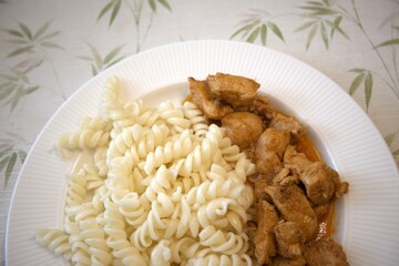 Traditional Hungarian chicken stew served with homemade pasta on white plate, close-up.