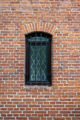Arched window with decorative grille on red brick wall.