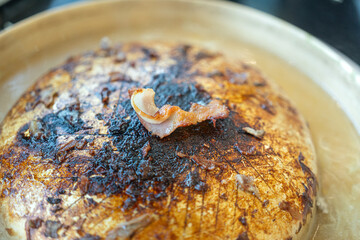 A piece of overburn pork fat from BBQ meal with smoke pan as background. Unhealthy risk food object, close-up with selective focus. 