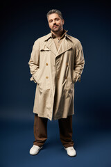 Handsome man in stylish trench coat poses confidently in a modern studio setting
