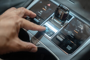 A car driver is activate on the electrical brake system switch on the modern car console....