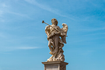 Angel statue with wings and cross on Ponte Sant Angelo bridge in Rome, Italy, against blue sky