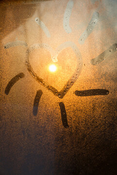 Cute heart drawn on steamy window around sun shining through