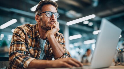 Young man working intently at laptop in modern office environment during daytime