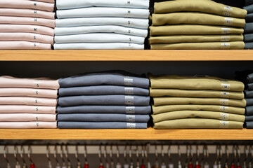Fototapeta premium Cloths in various base color tone are folded on the shelf in clothing store. Fashion cloth object photo, close-up and selective focus. 