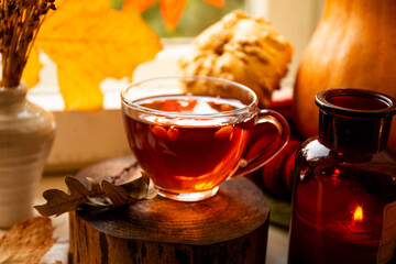 Mug of hot tea with sea buckthorn and autumn decorations on the autumn window. Autumn and fall cozy postcard