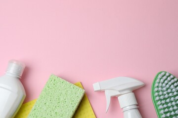 Flat lay with cleaning supplies including bottle, sponge, spray on pink background. Top view