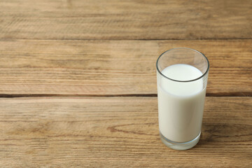 Fresh milk in a glass at light wooden table in kitchen, closeup