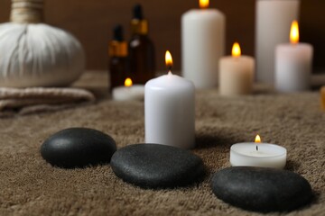 Burning candles, spa stones on fabric background, close up