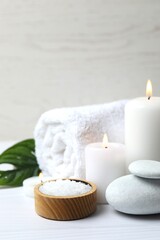 Vertical view of spa composition with white towel, salt and candles on wooden table. Spa and beauty treatments