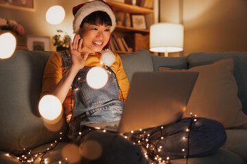 Woman wearing Santa hat having video call using laptop computer while celebrating Christmas at home