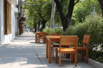Obraz premium modern stylish cafe setting on sunny street with contemporary wooden tables and chairs