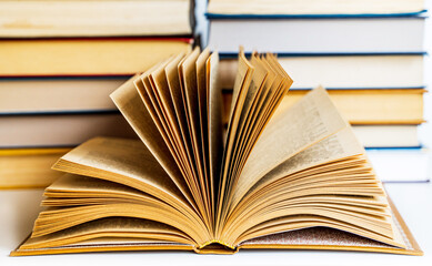 two large stacks of old, tired, worn-out books of yellow, blue, brown colors lie, and in front of them is an open book with flying yellowed pages
