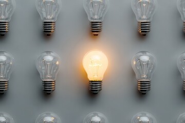 Single Illuminated Light Bulb Glows Among Many Unlit Bulbs on Grey