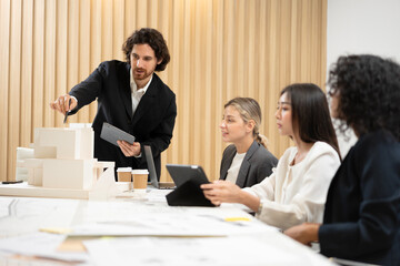 Businessman leading a meeting and presenting a housing project plan using a scale model to his colleagues in a modern office
