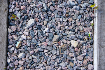 Image shows a top-down view of decorative gravel within a wooden-bordered area, with small green...
